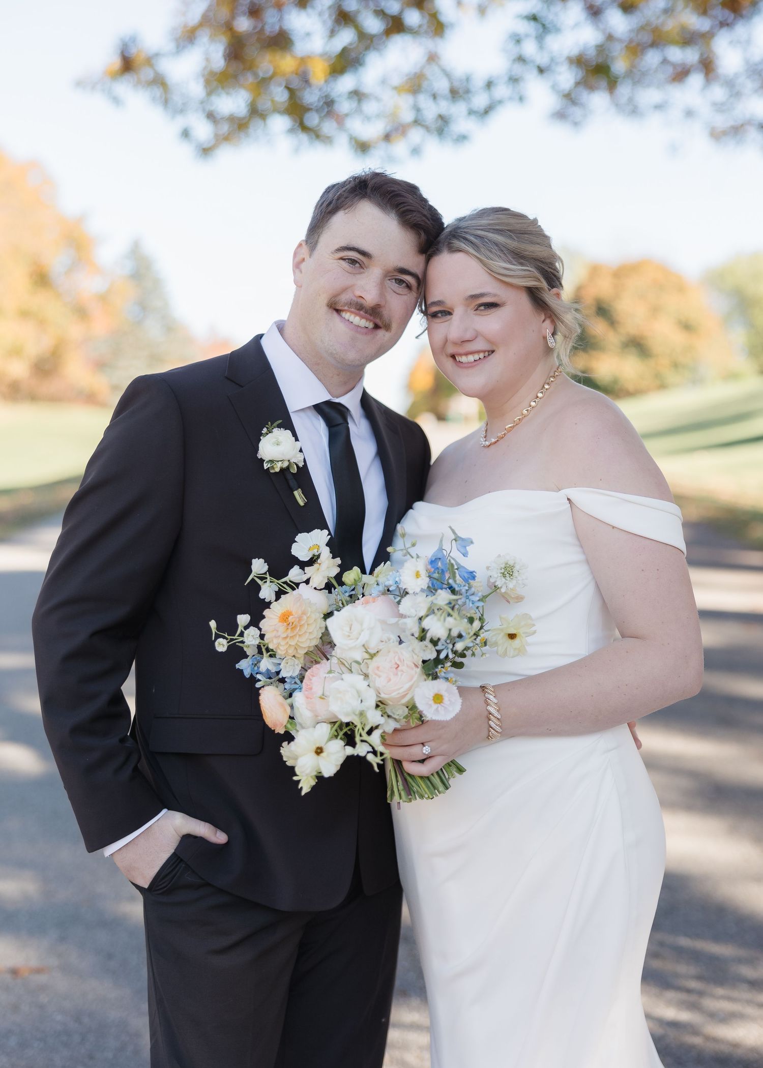 Wedding portrait of couple with elegant white and blue floral bouquet on autumn day.