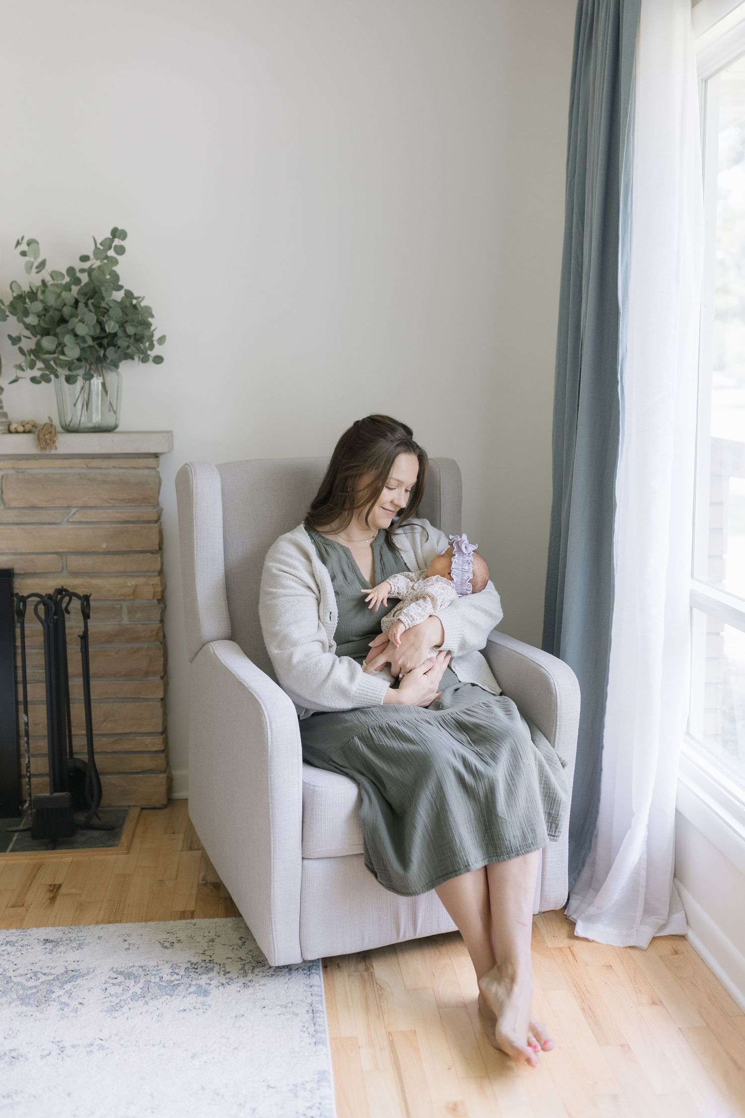 A parent sits in a white armchair by a window, holding and feeding a baby in three similar poses.
