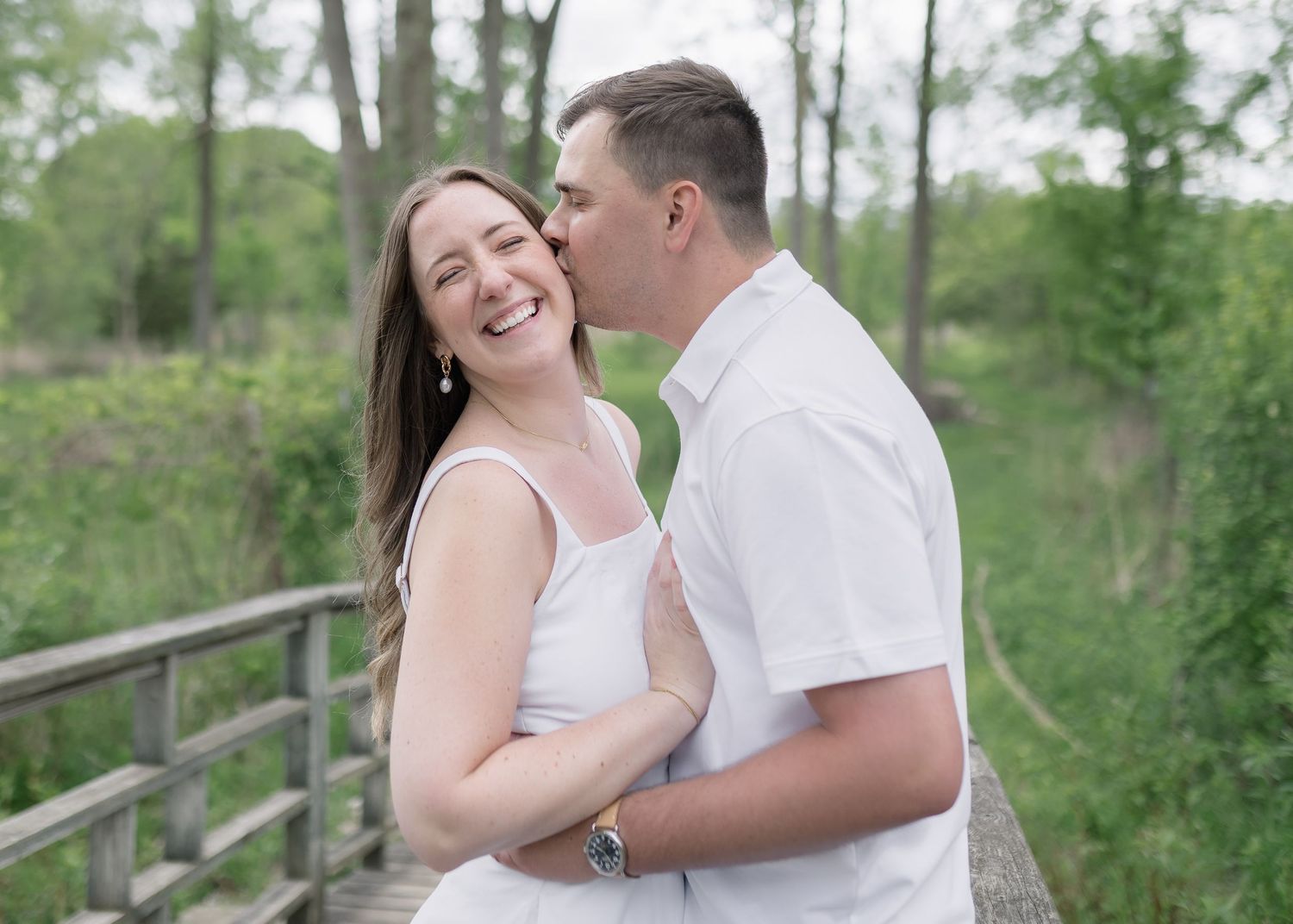A couple in white outfits share joyful moments together while posing outdoors in a natural setting.