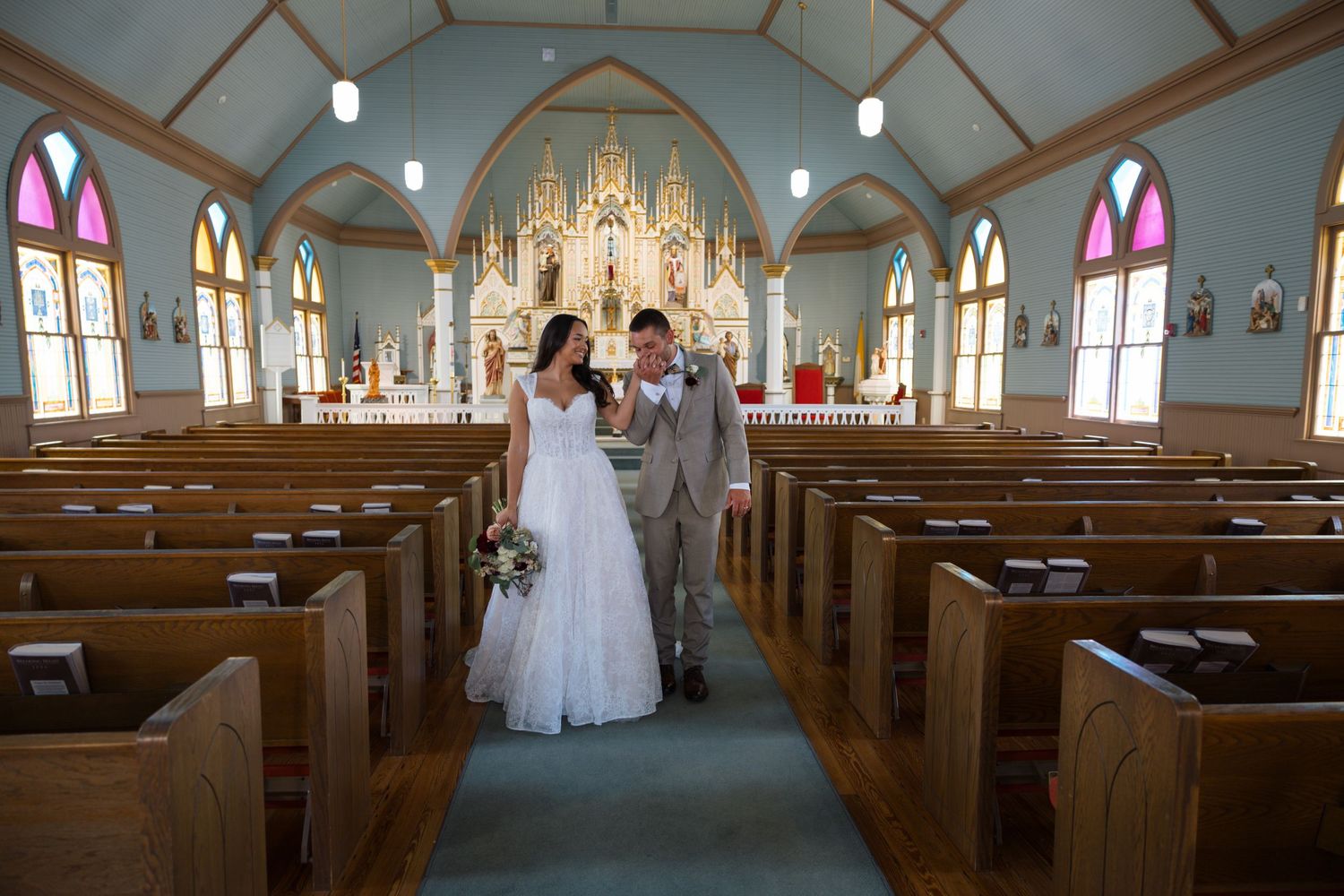 Bride and groom walk down the aisle of a beautiful historic church with colorful stained glass windows.