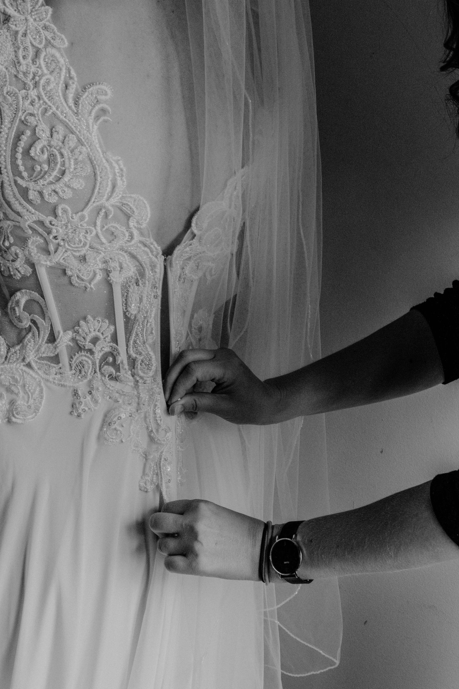 Black and white photo of hands adjusting the delicate lace details on an elegant white wedding dress.