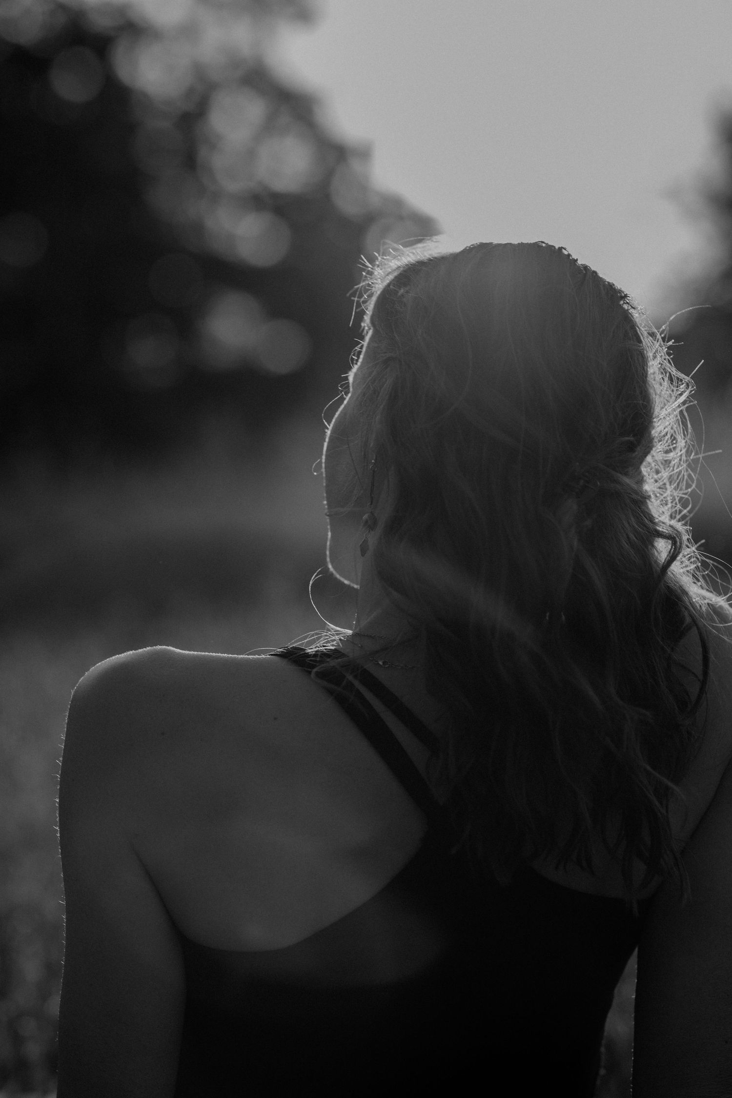 Silhouette of a person with long wavy hair in a tank top viewed from behind in black and white.