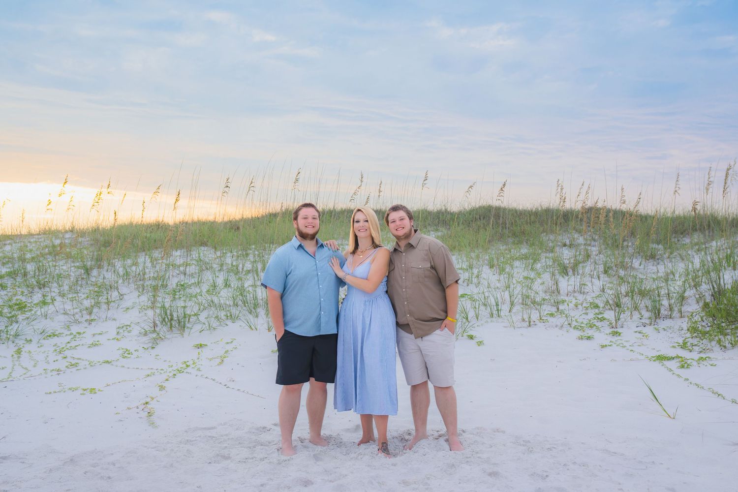Three people pose together on a white sand beach at sunset with sea oats in the background.