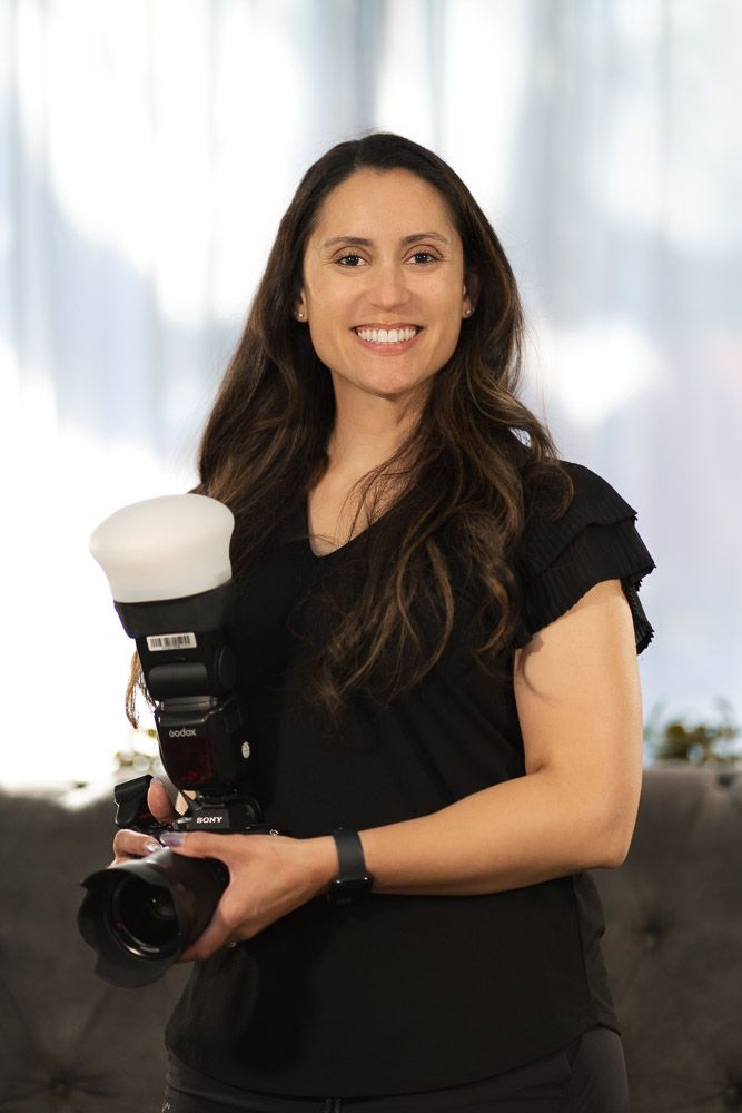 Professional female photographer smiling while holding Sony camera with flash indoors.