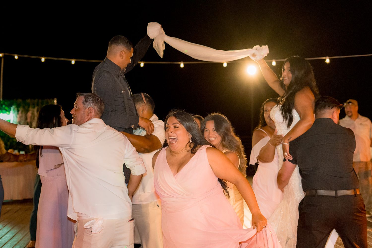 Guests dancing joyfully at an outdoor wedding reception at night, with string lights illuminating the festive celebration.