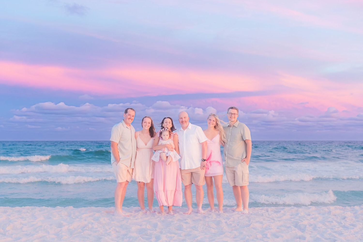 Family of six poses on a beach with a breathtaking pink and purple sunset sky.