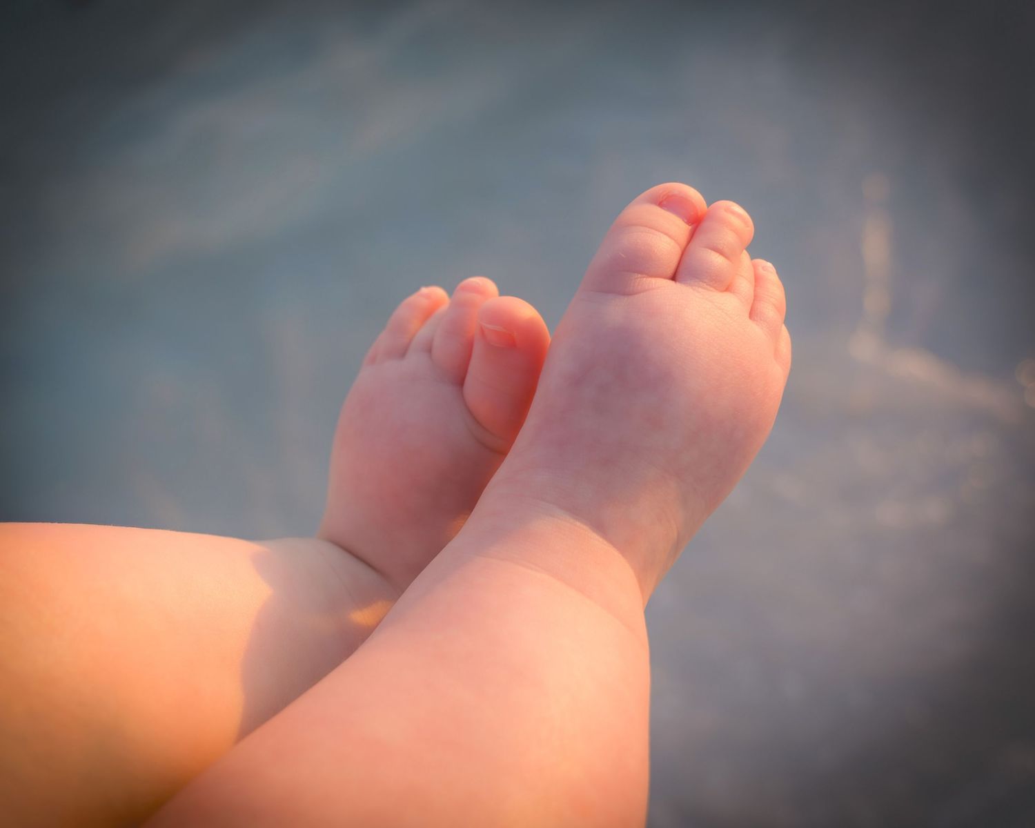 Close-up of adorable baby feet resting against a soft blue background in warm sunlight.