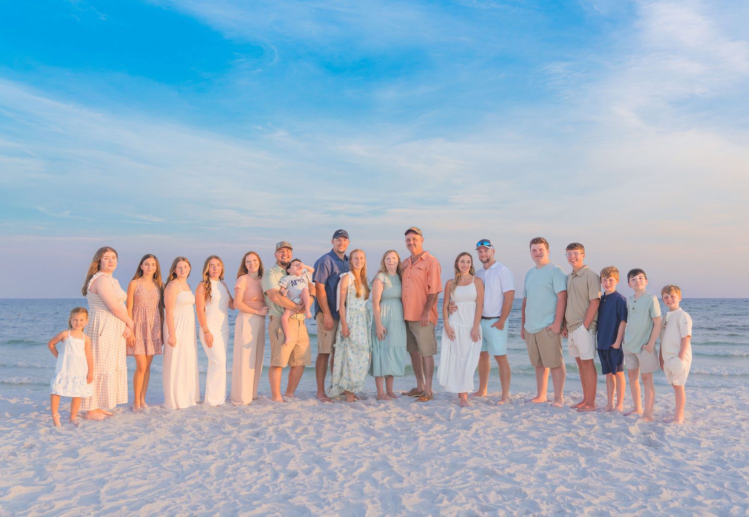 Large family group posing together on a white sand beach at sunset with a blue sky backdrop.
