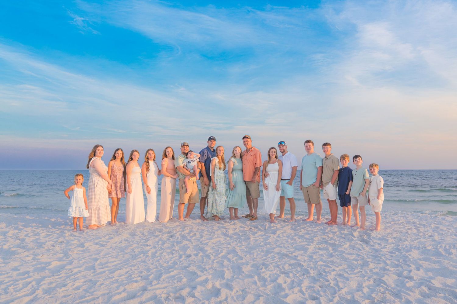 Large family group posing together on a white sand beach at sunset with a beautiful blue sky backdrop.