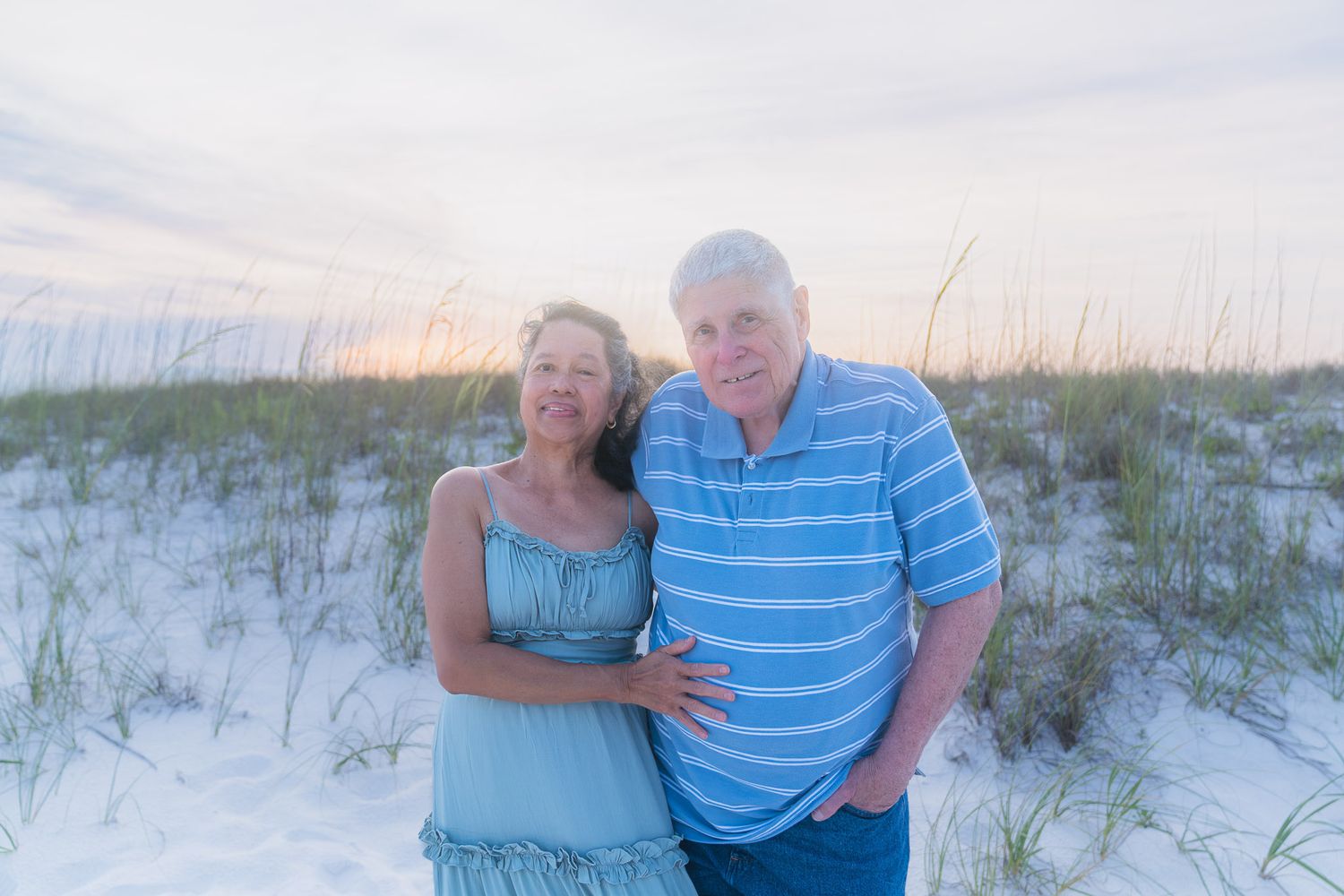 Couple smiling together on a white sand beach at sunset with sea oats in the background.