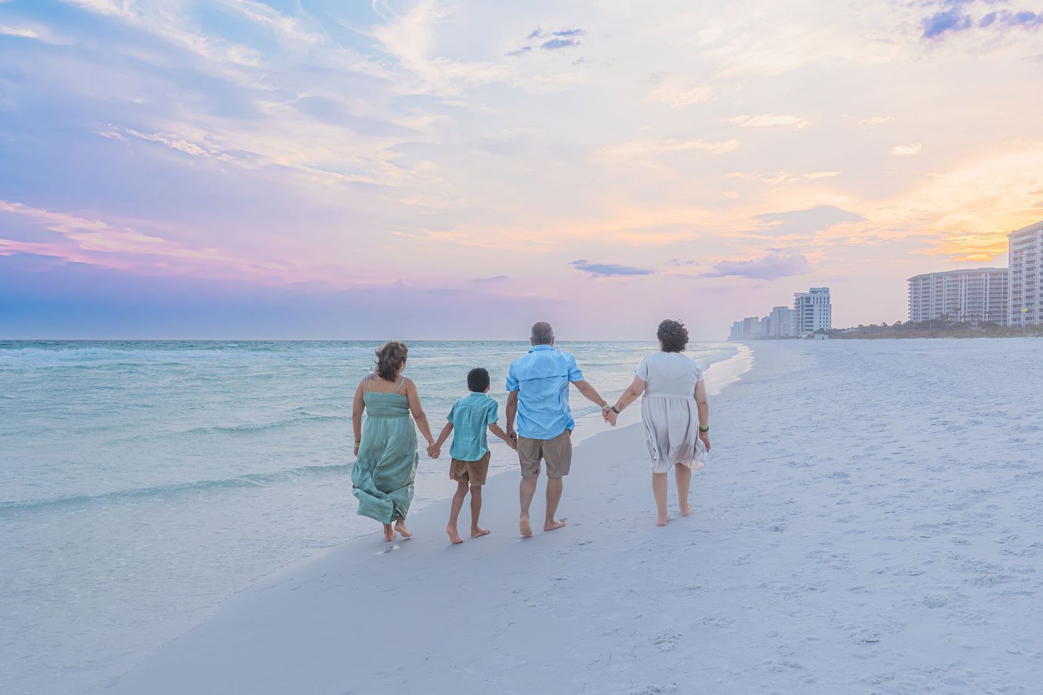 Family of five holding hands walking along a serene beach at sunset with pastel skies and calm turquoise waters.