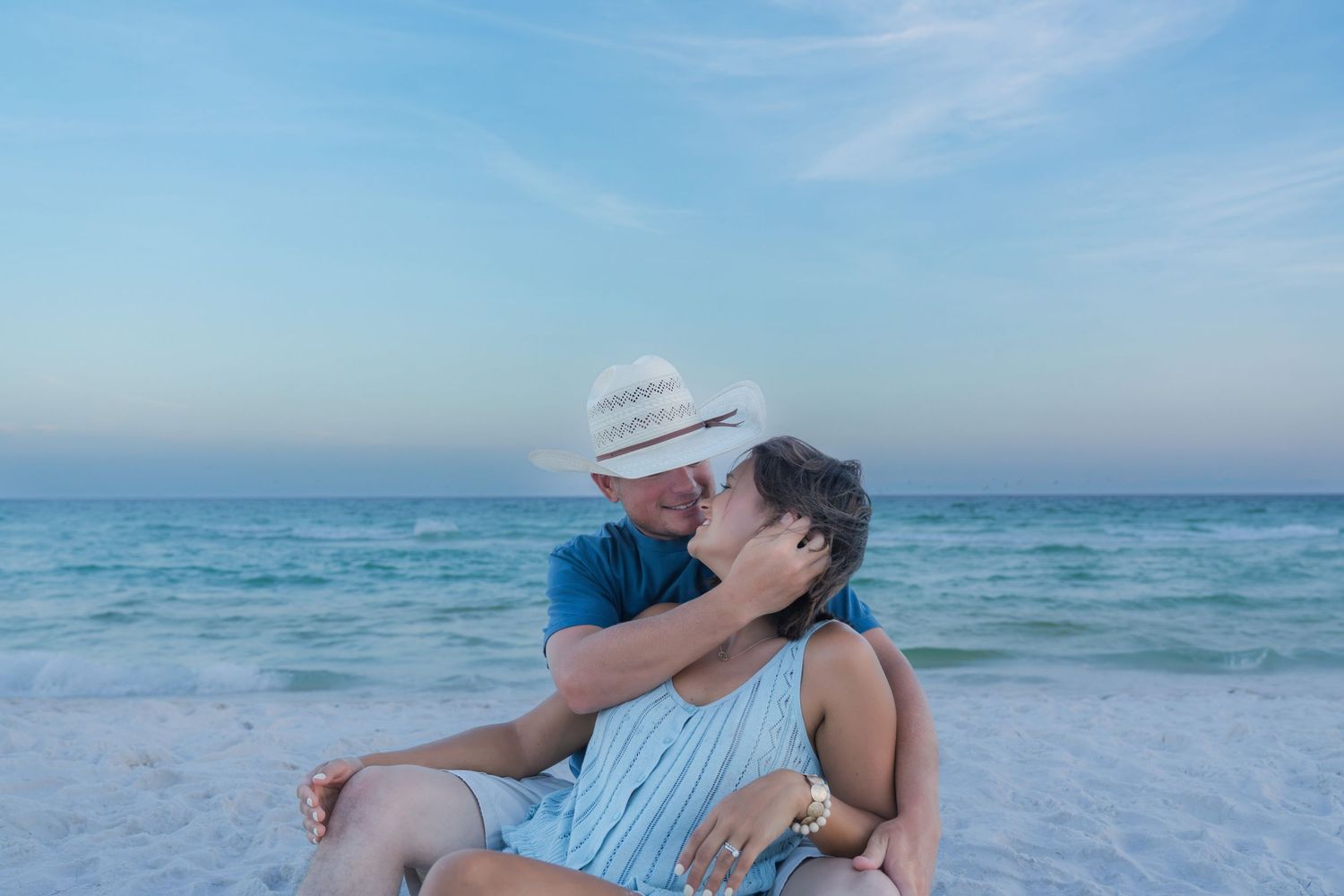 Romantic couple sharing a kiss on a sandy beach with turquoise ocean waves in the background.