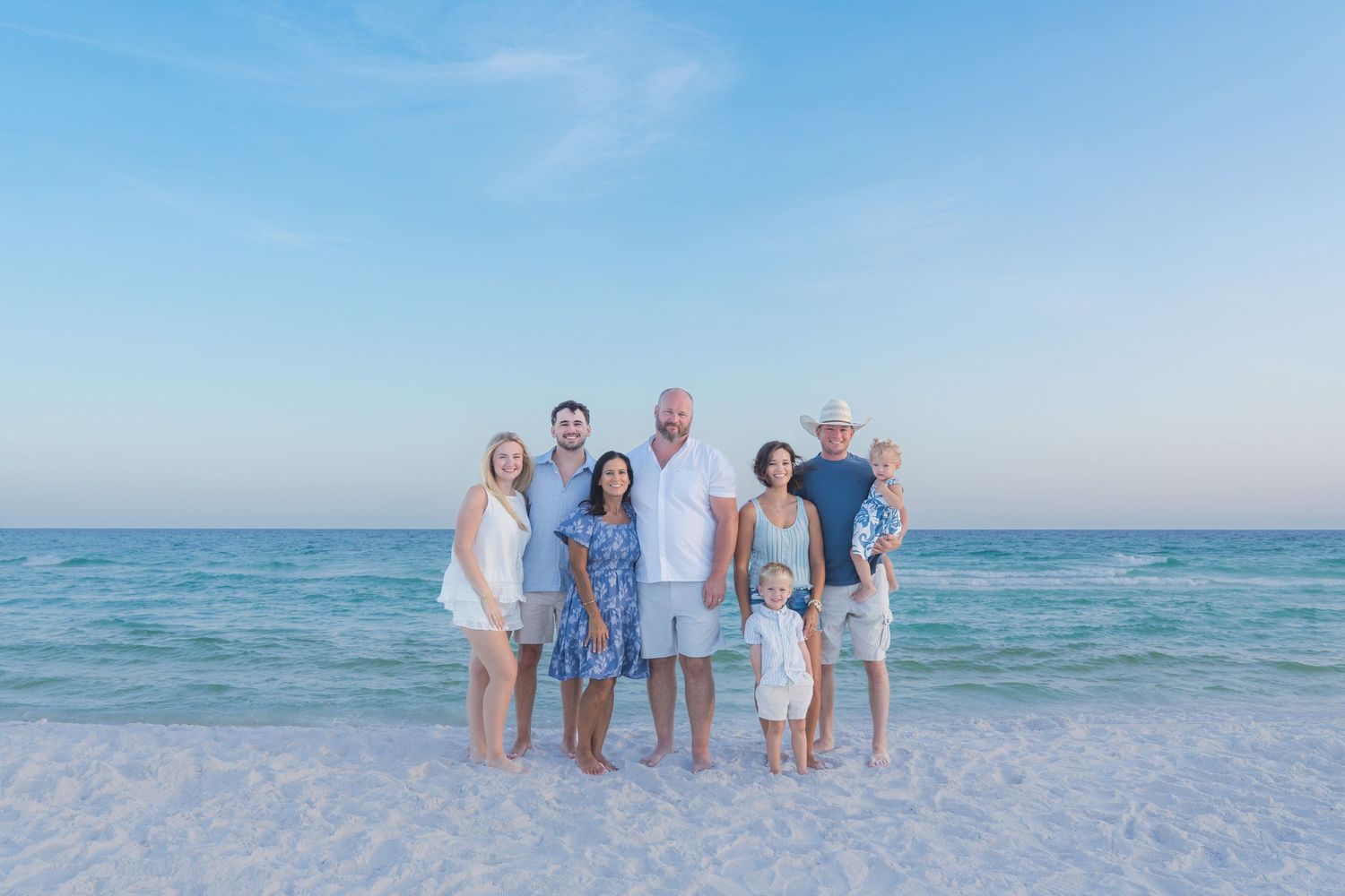 Family group photo on a white sand beach with turquoise water, posing together under a clear blue sky.