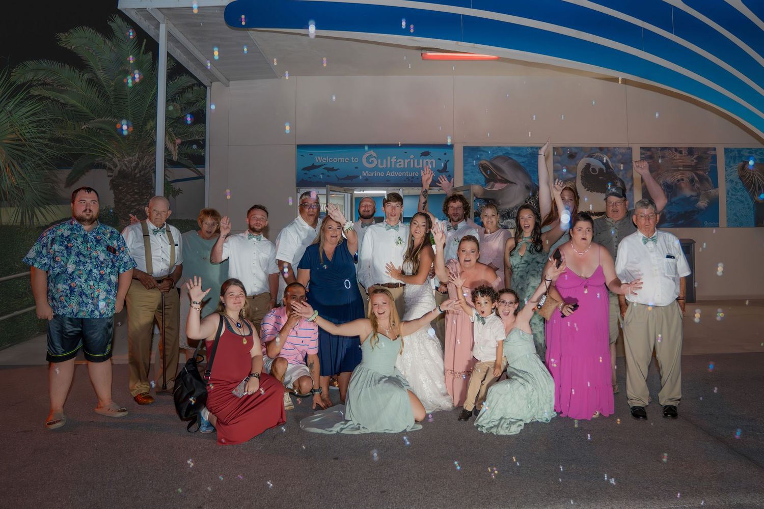 Wedding party group photo with bubbles outside aquarium venue celebrating with bride and groom.