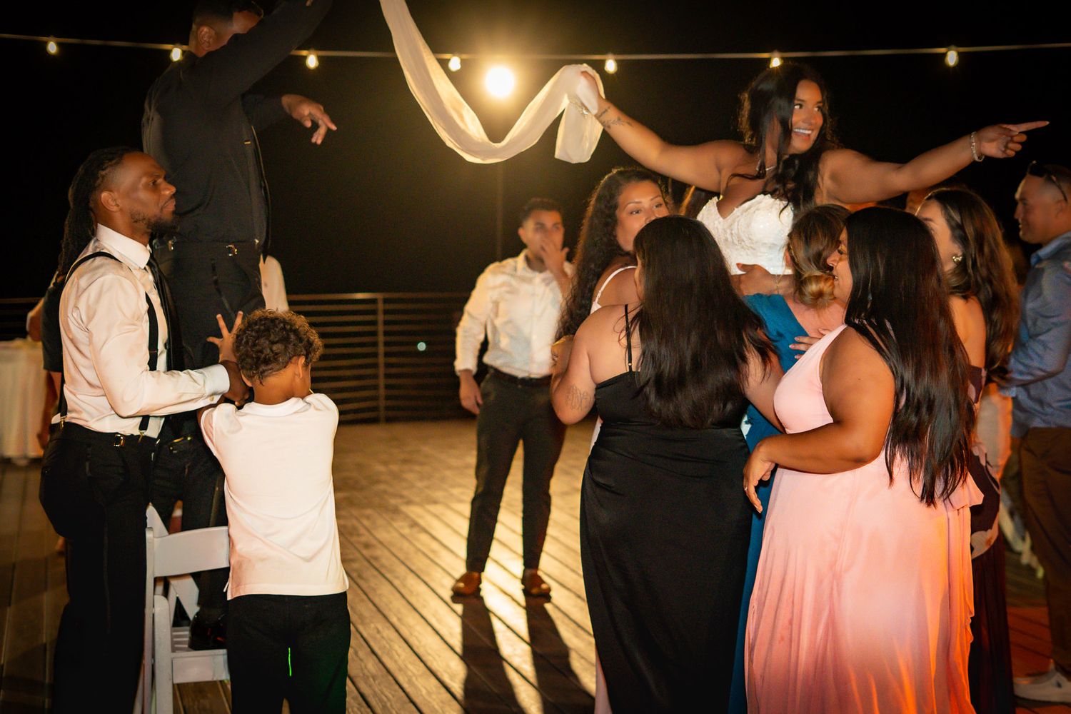 Guests dancing and celebrating at an outdoor wedding reception on a deck at night.