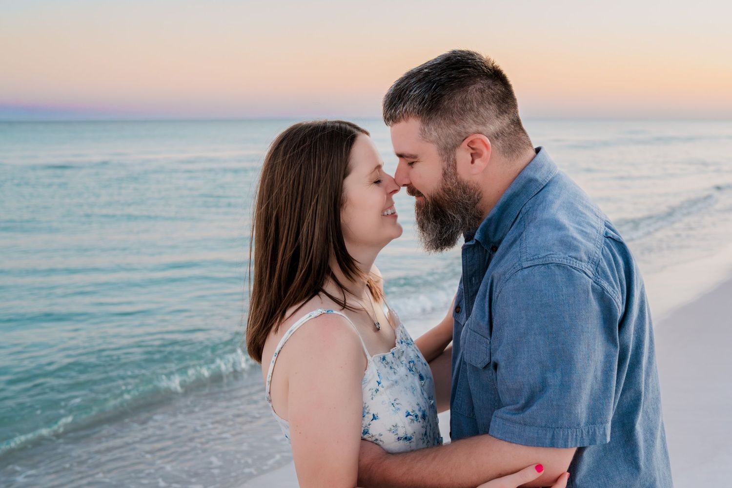 Couple sharing a romantic moment on the beach at sunset, touching foreheads near the ocean.