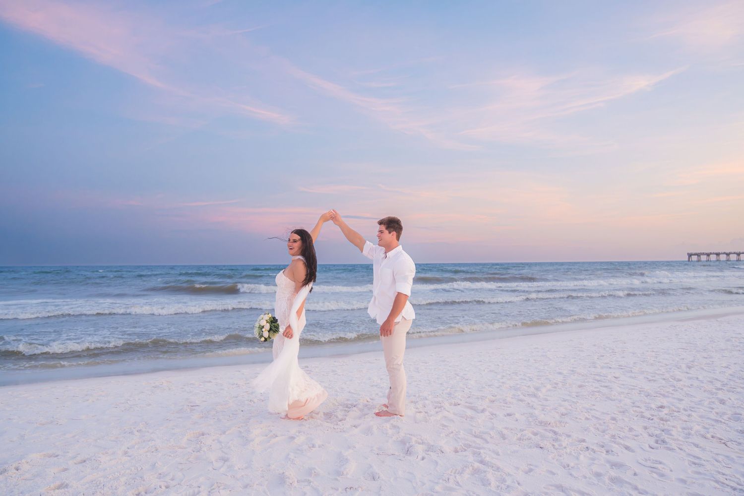 Bride and groom dance on beach at sunset during romantic seaside wedding ceremony.
