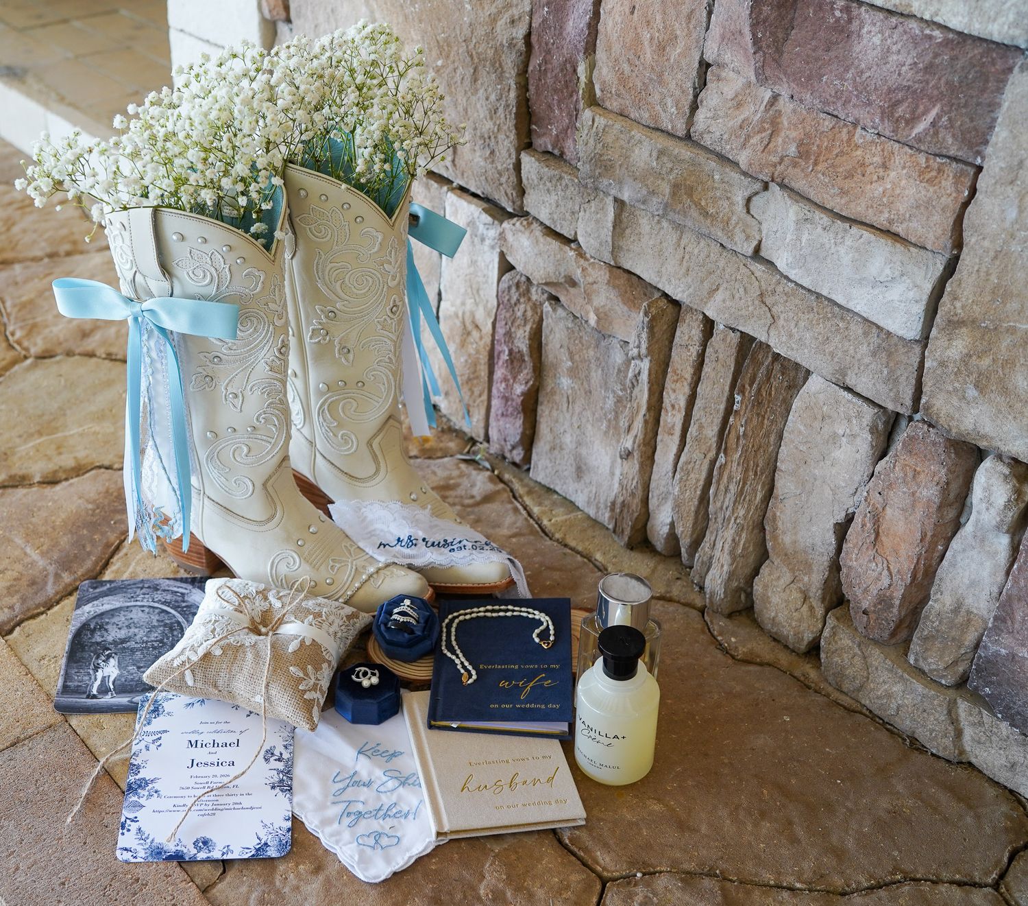 White cowboy boots with baby's breath flowers displayed with wedding stationery and accessories on stone surface.
