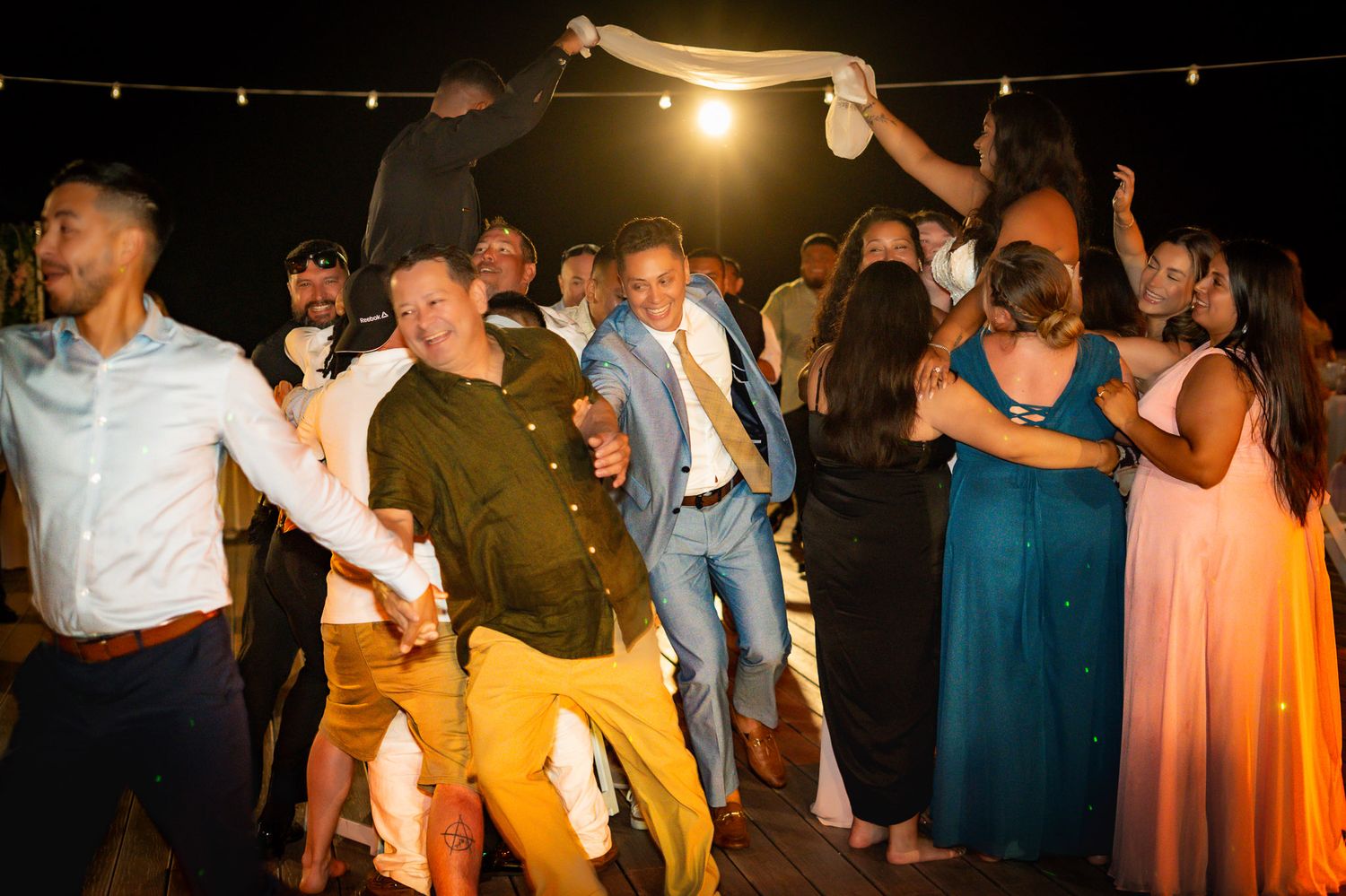 Wedding guests dancing joyfully at an outdoor evening reception celebration.