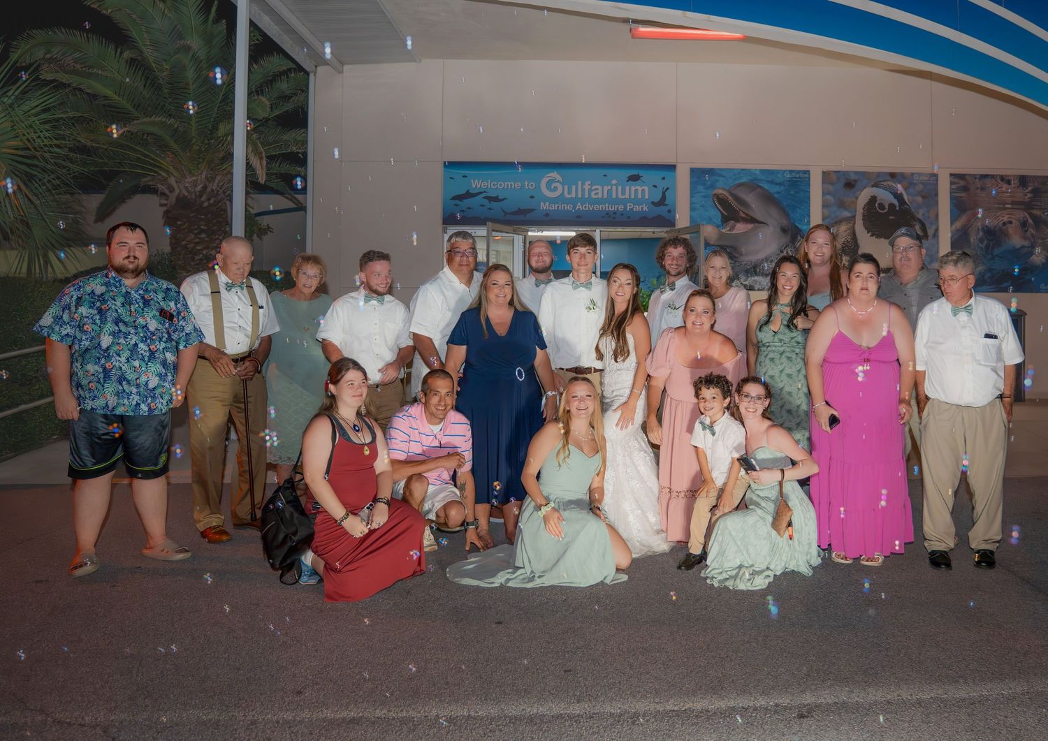 Large wedding party group photo posed outside aquarium venue at night after reception.