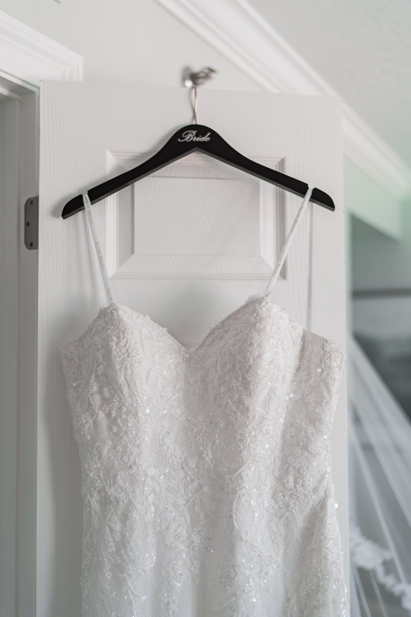 White lace bridal gown hanging on a black Bride hanger on a white door before the wedding ceremony.