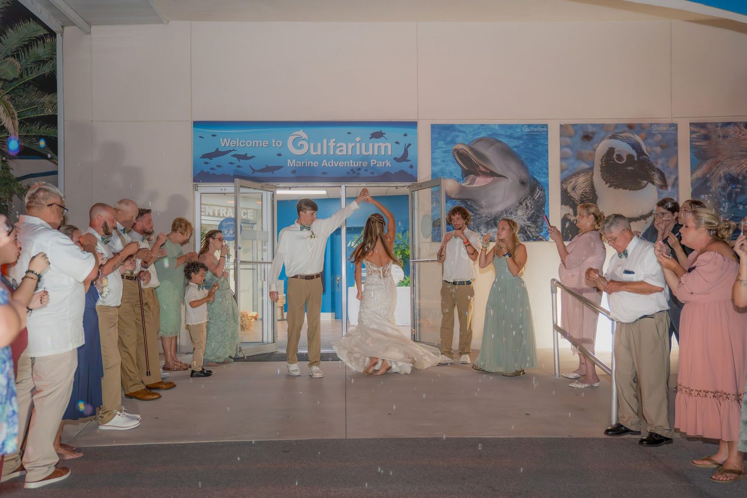 Couple celebrates wedding at Gulfarium Marine Adventure Park entrance with guests cheering and confetti.