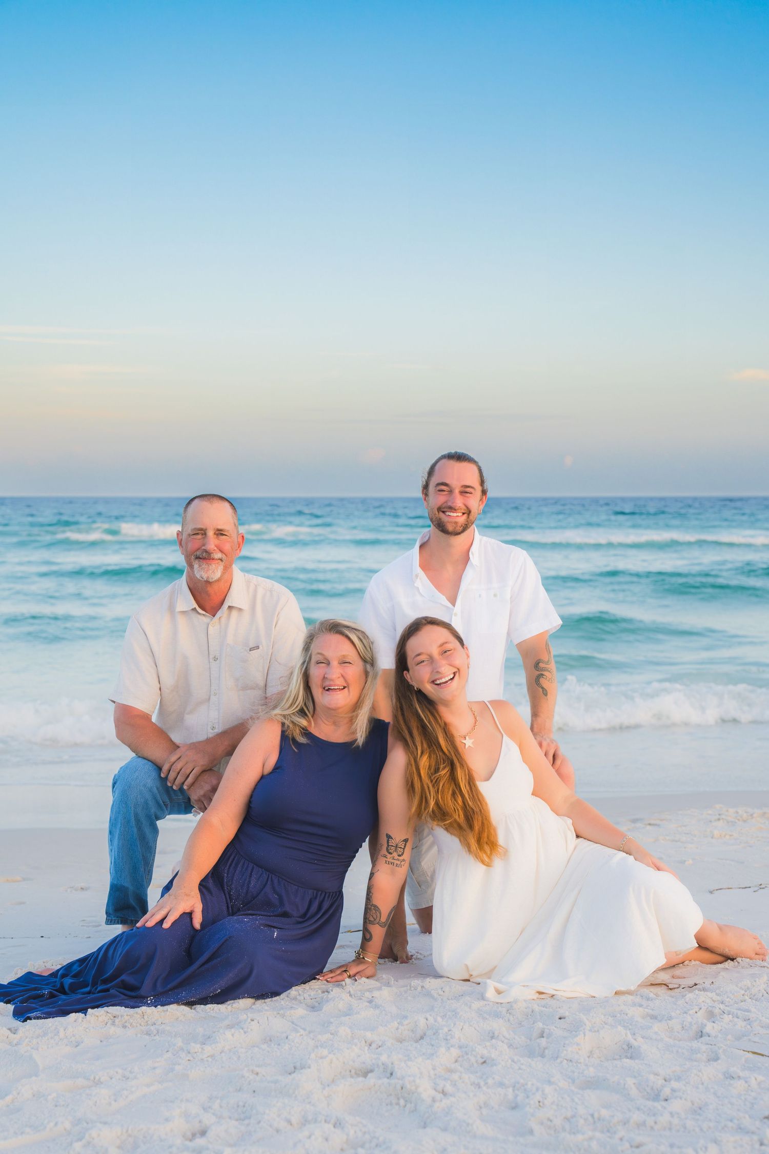 Family of four smiling together on a white sand beach at sunset with turquoise ocean waves in the background.