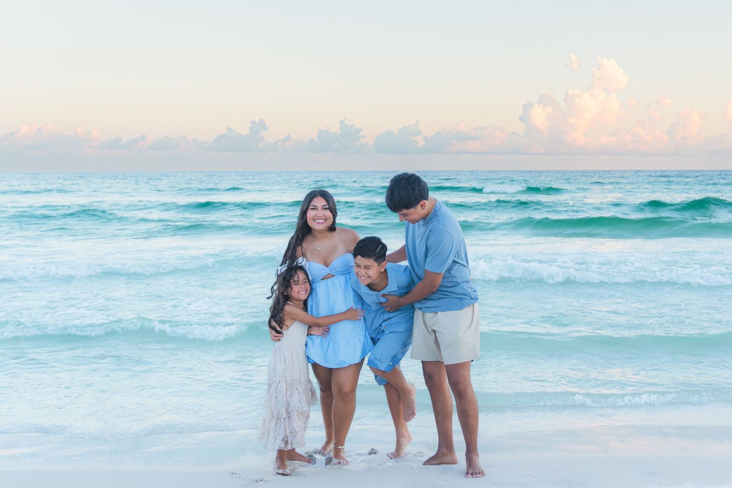 Family of four posing on a sandy beach at sunset with turquoise ocean waves in the background.