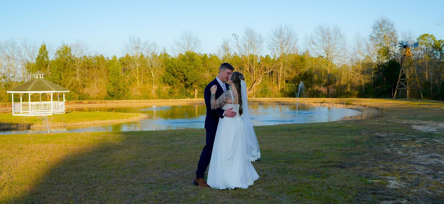 Bride and groom share a tender moment together near a serene pond at outdoor wedding venue.