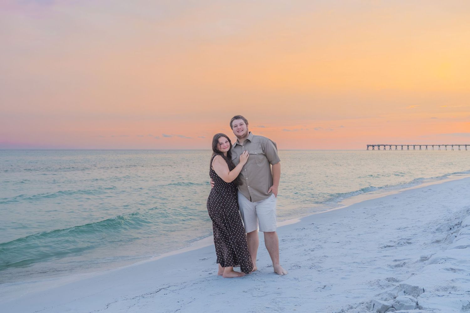 Romantic couple embracing on a white sand beach during a vibrant pink and orange sunset.