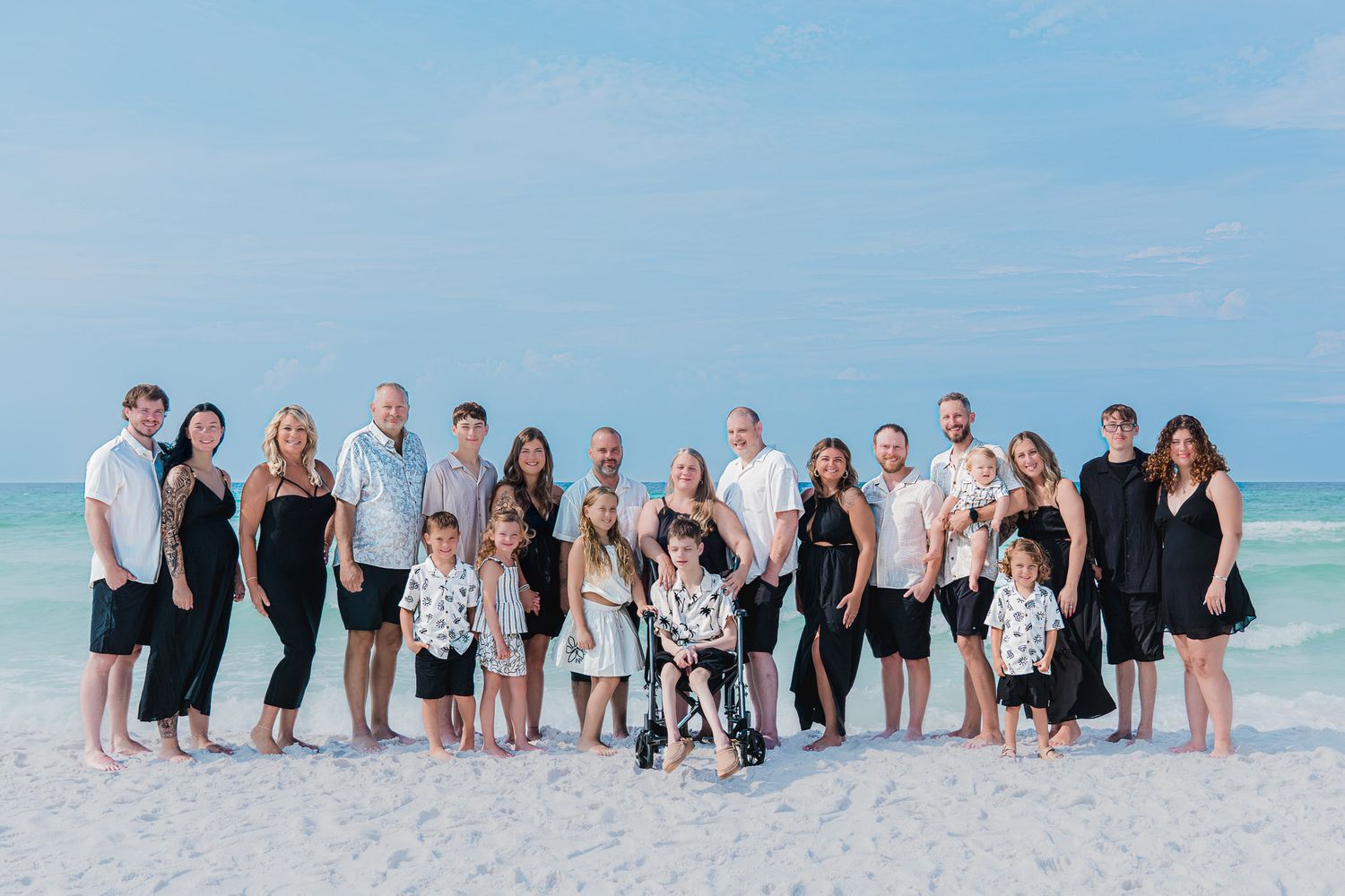 Large family group photo on a white sand beach with turquoise water, posing together for a portrait.
