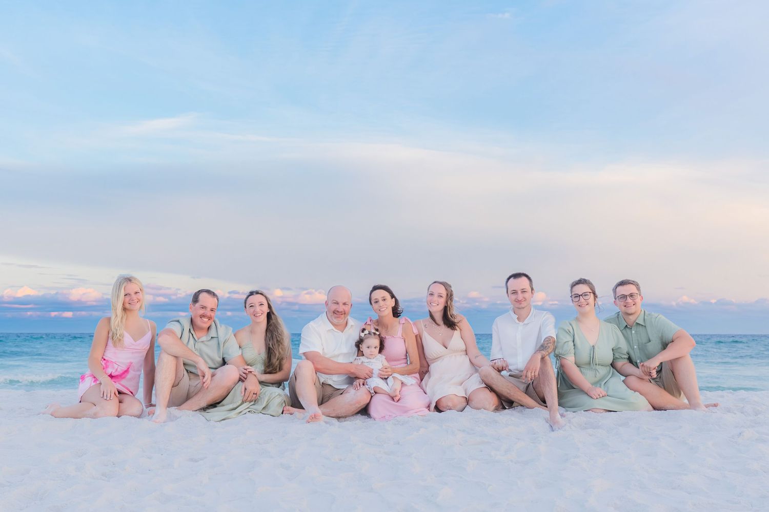 Large family group portrait on white sand beach at sunset, wearing coordinated pink and green outfits.