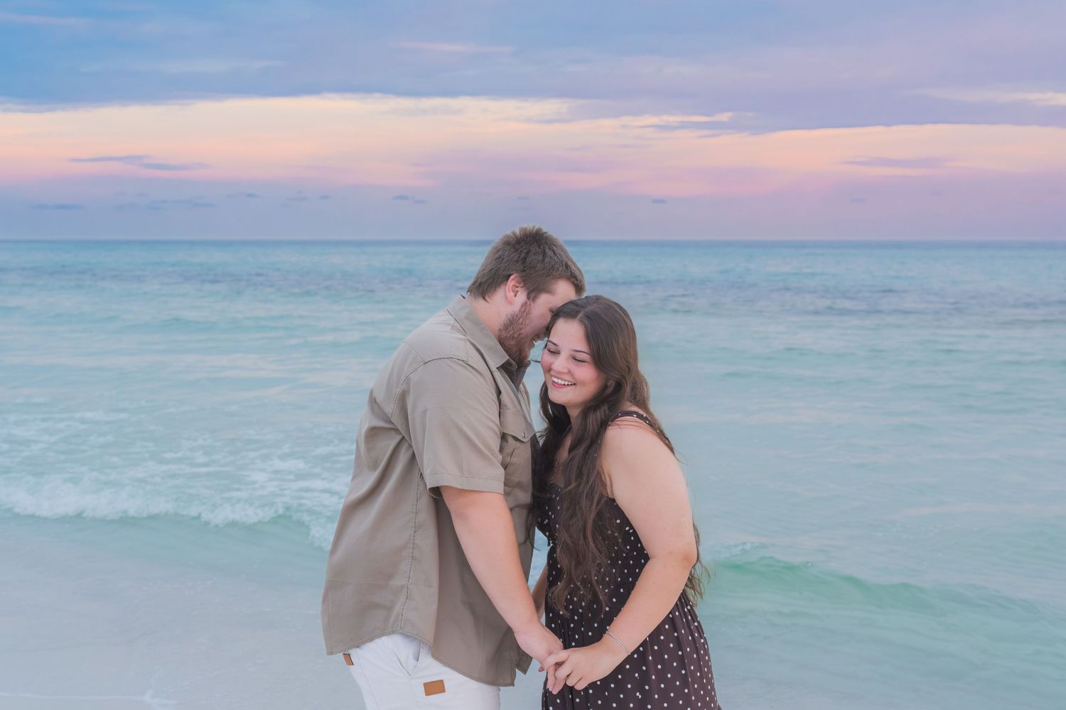 Couple holding hands smiling at sunset on a white sand beach with turquoise water.