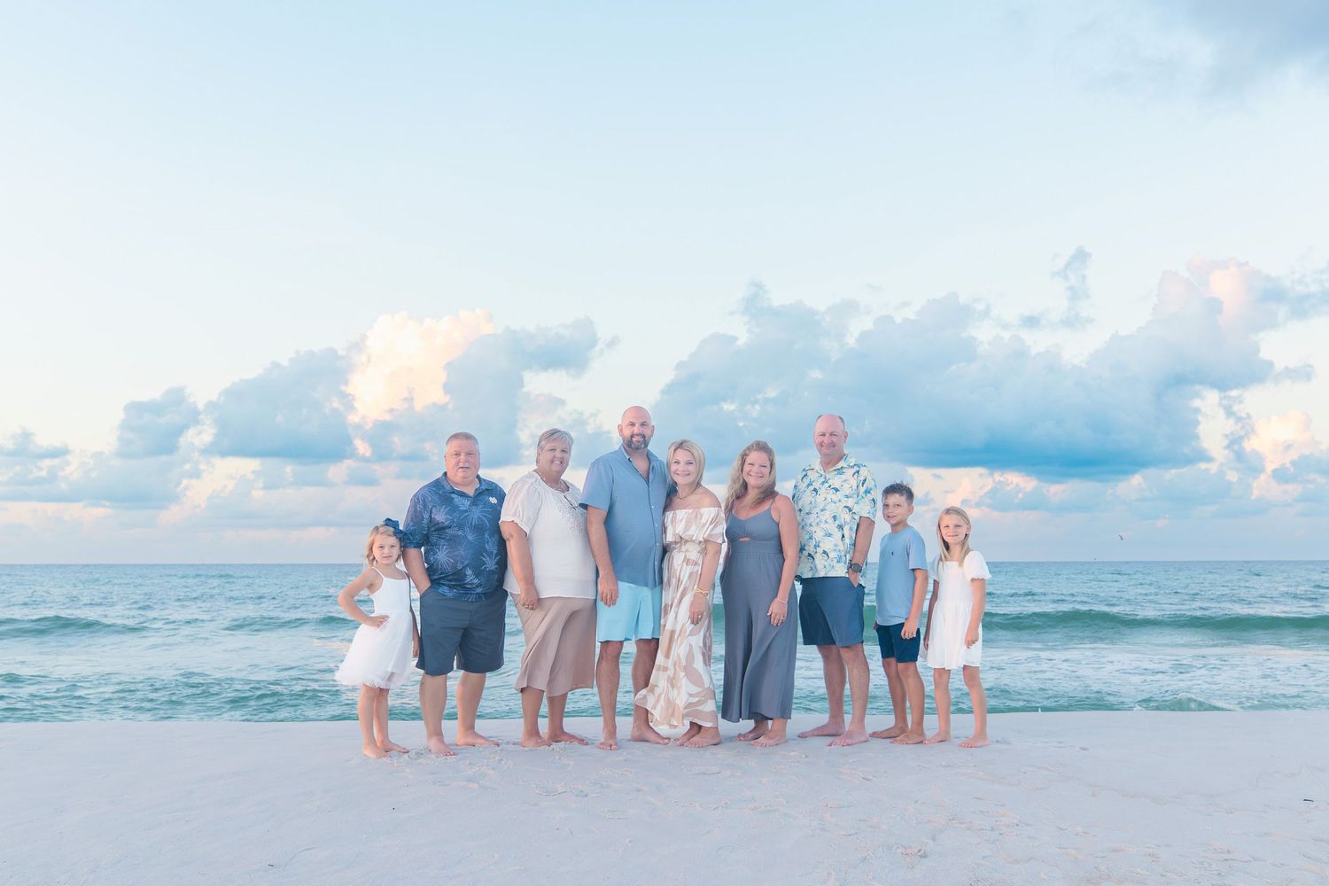 Family group photo on a sandy beach at sunset with calm ocean waves and pastel cloudy sky in the background.