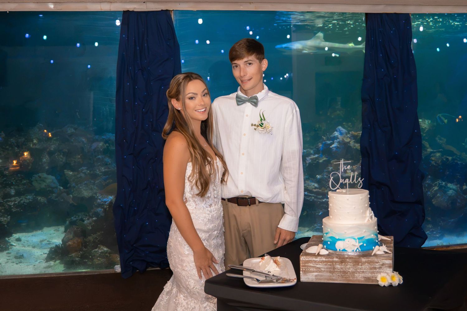 Bride and groom cut their wedding cake in front of a large aquarium tank at their reception.