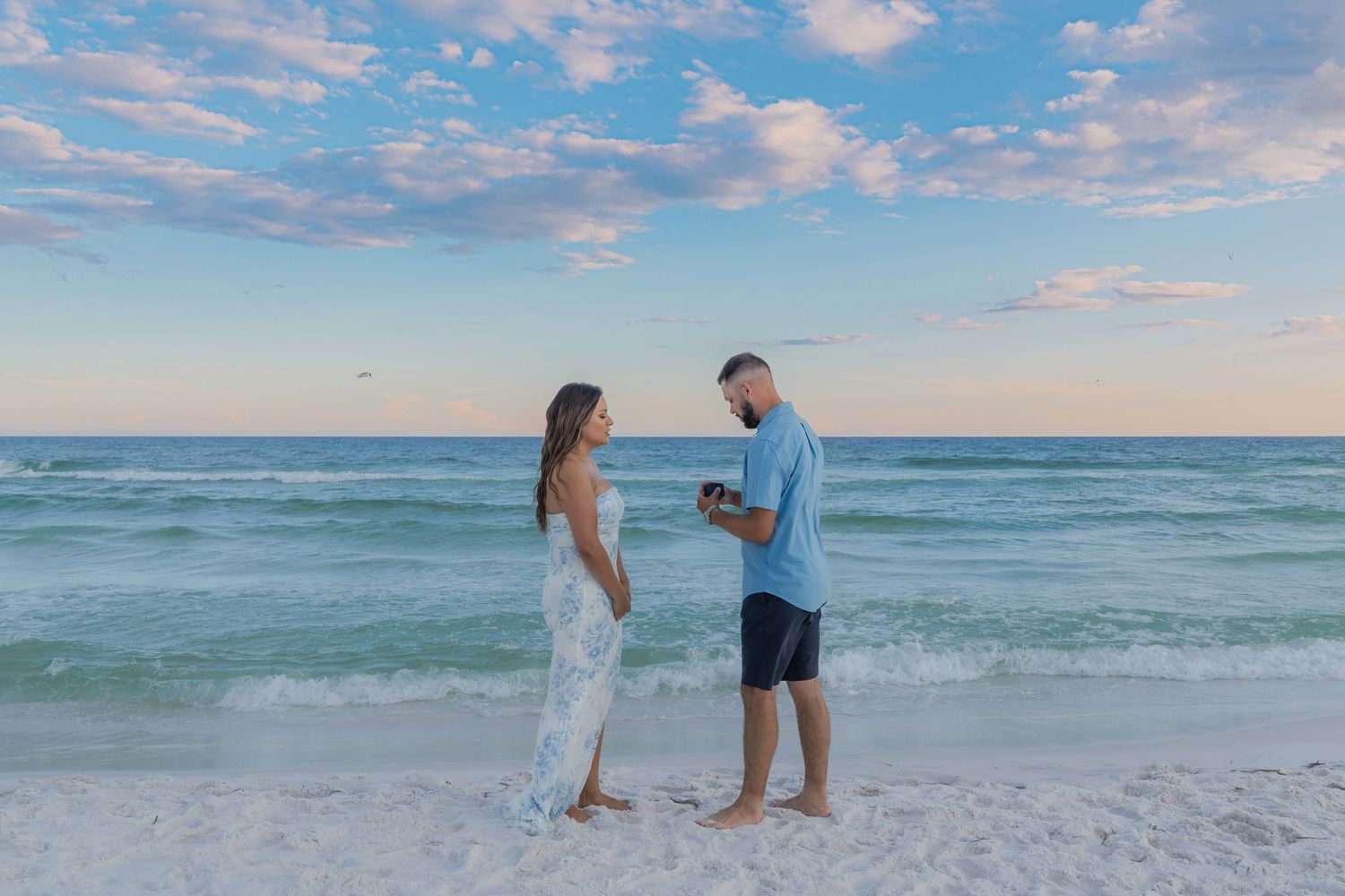Couple sharing a romantic moment on a white sand beach at sunset with turquoise ocean waves behind them.