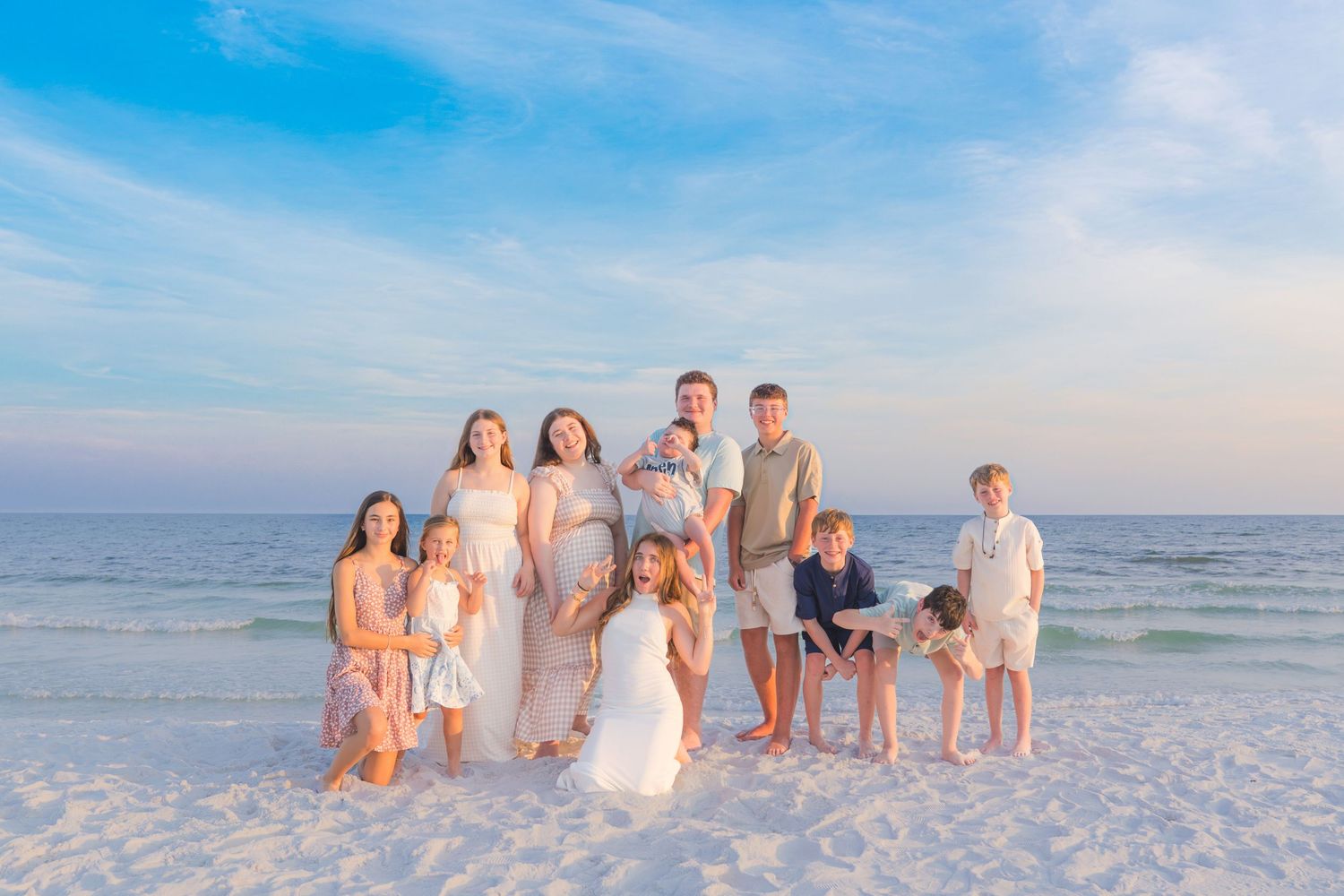 Large family posing together on a white sand beach at sunset with calm ocean waves and blue sky.