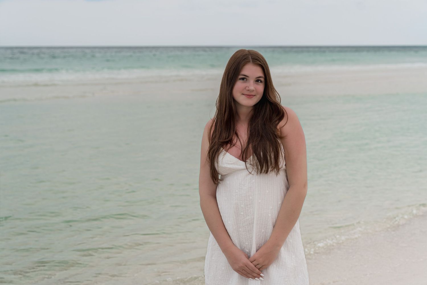 Young woman in white dress smiling on a tropical beach with turquoise ocean water in the background.