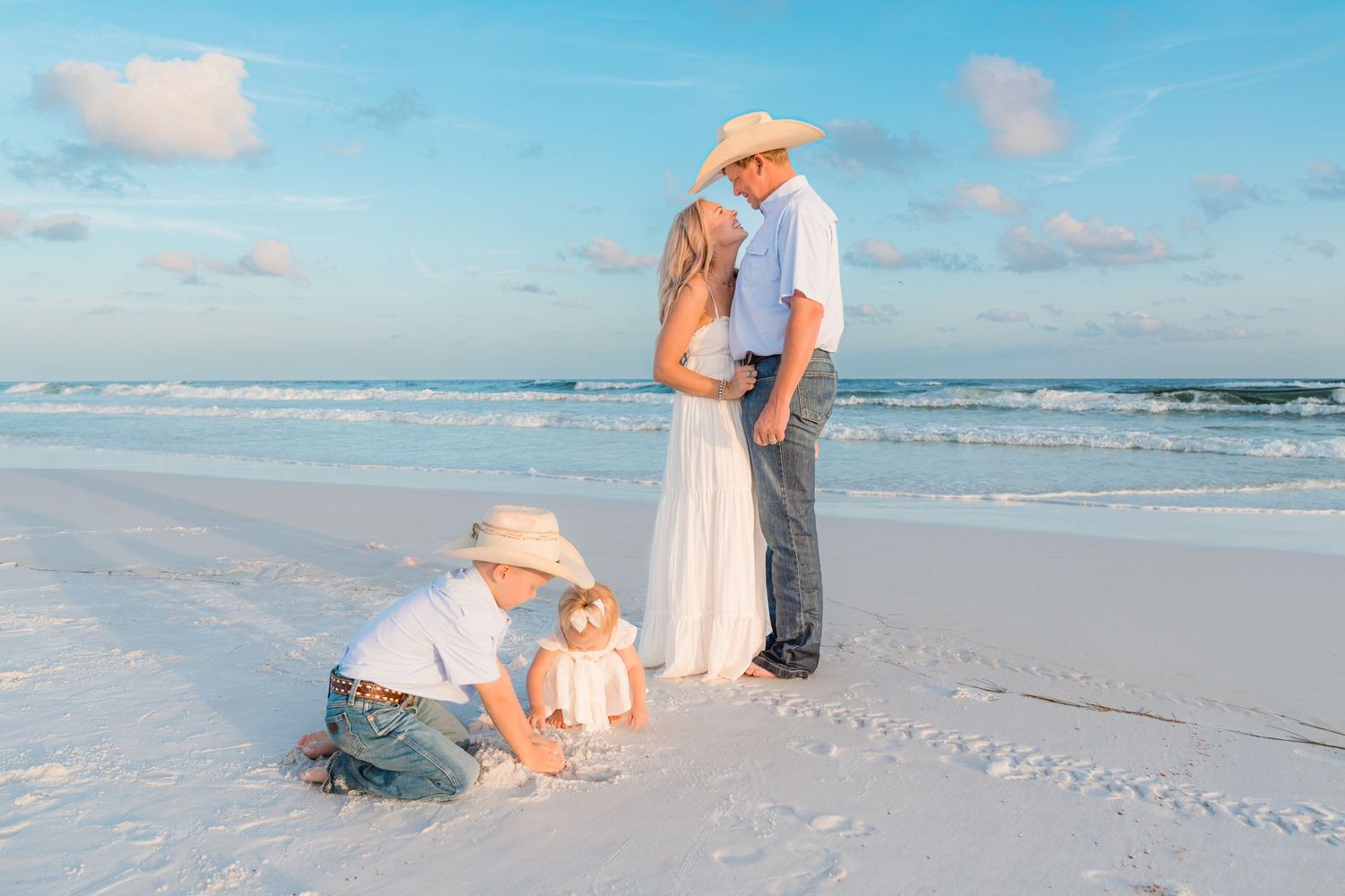 Family of four enjoying a beach day, parents sharing a romantic moment while children play in the sand.