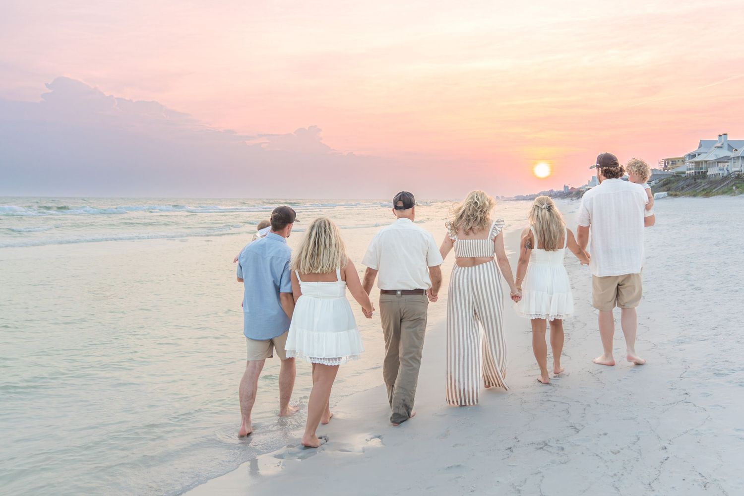 Family of six walks hand-in-hand along a white sand beach at sunset in matching white outfits.