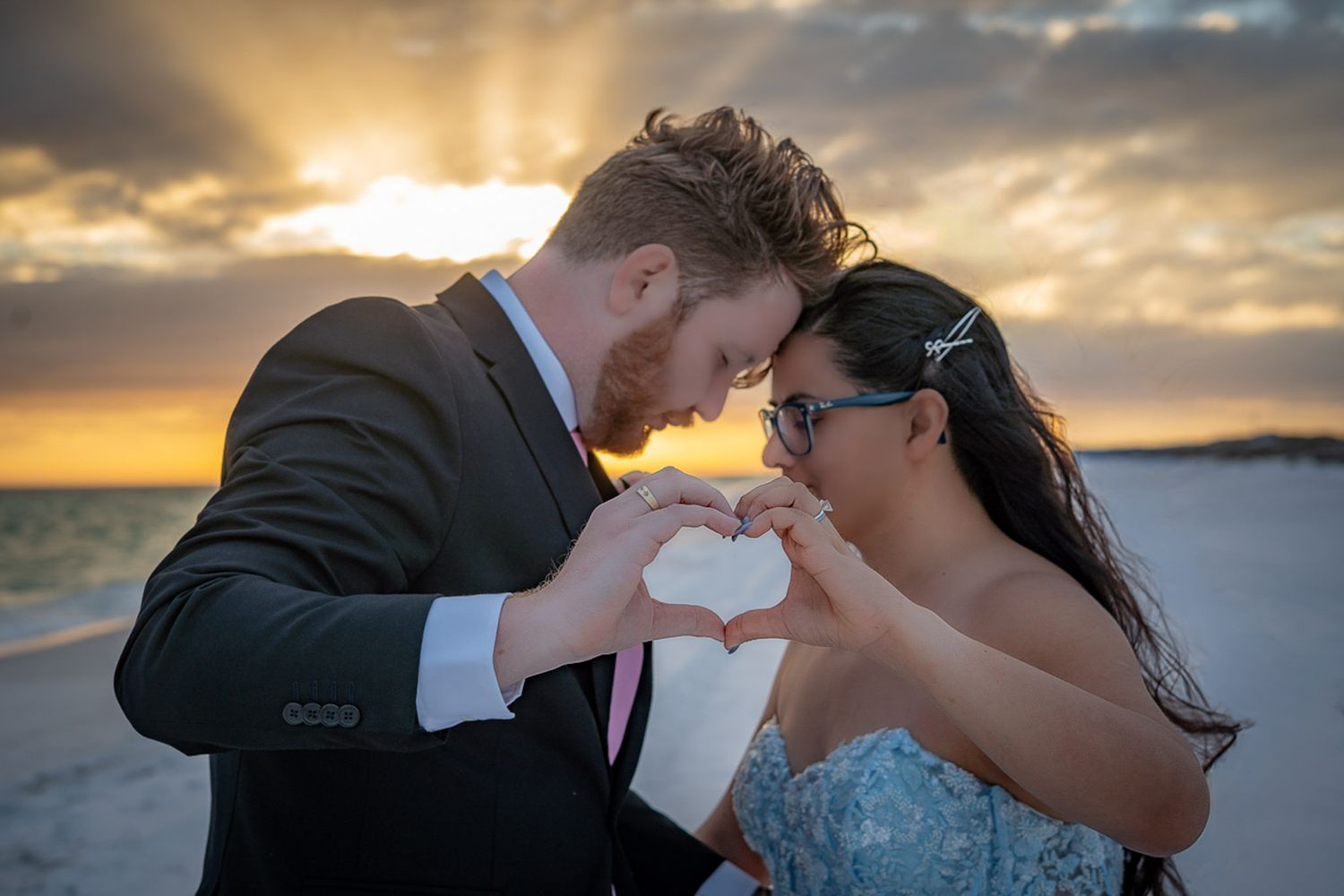 Bride and groom making a heart shape with their hands at sunset on a beach wedding.