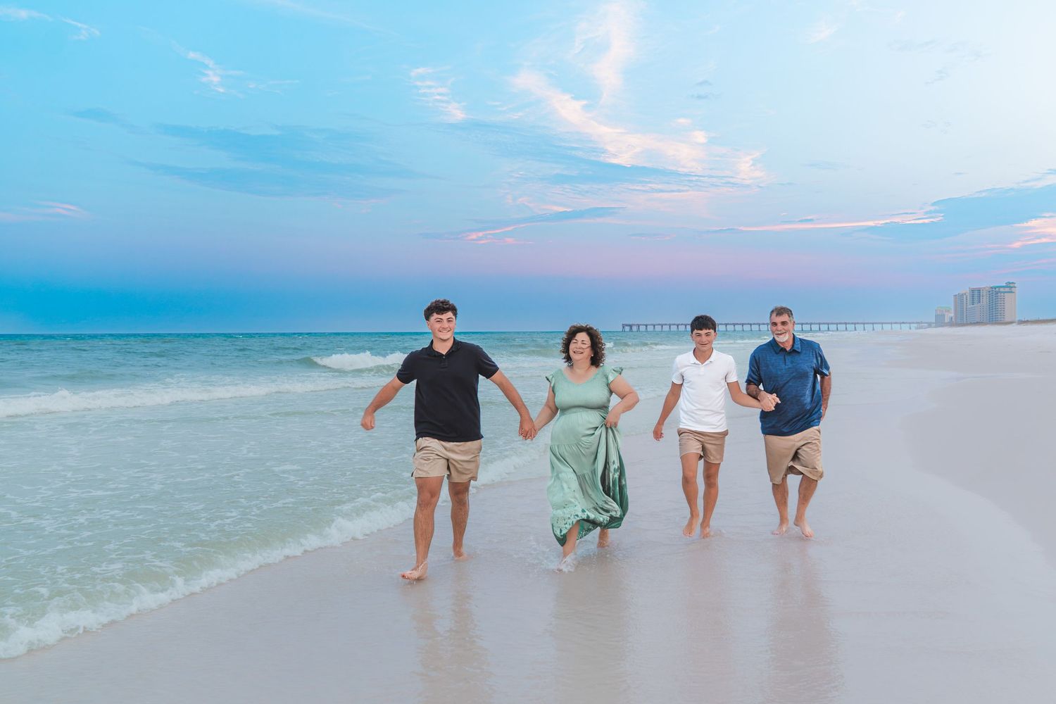 Family of four walking on a beach at sunset with turquoise water and colorful sky in background.
