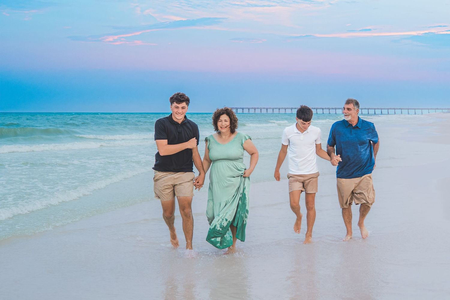 Family of four walking along a beautiful beach at sunset, waves gently lapping the shore.