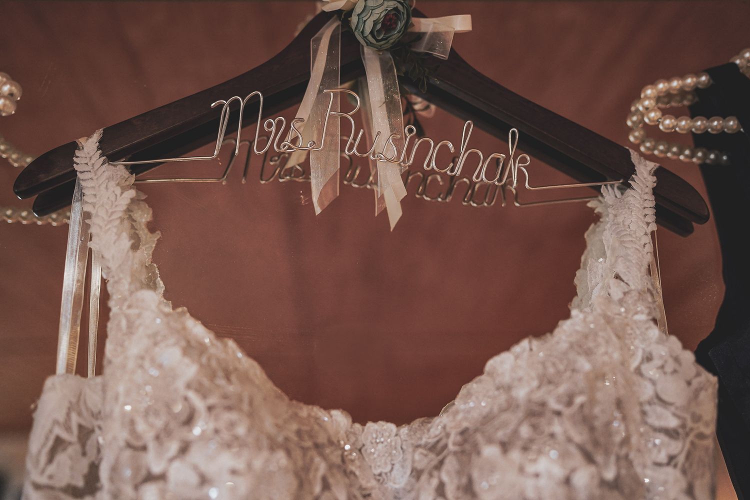 Elegant lace wedding dress hanging on a personalized Mrs. Russinchak wooden hanger against a warm backdrop.