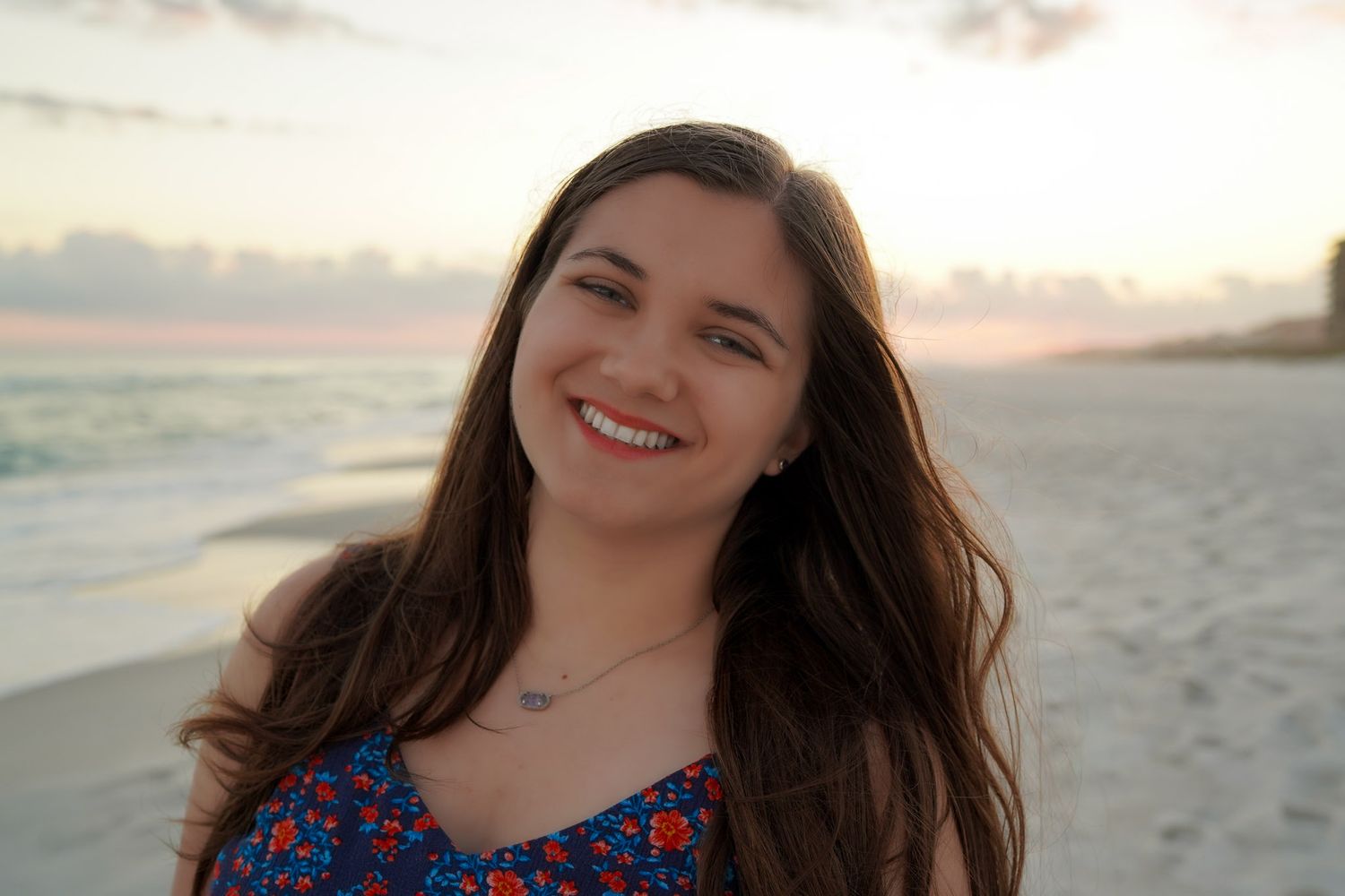 Young woman smiling on a beach at sunset with ocean waves in the background.