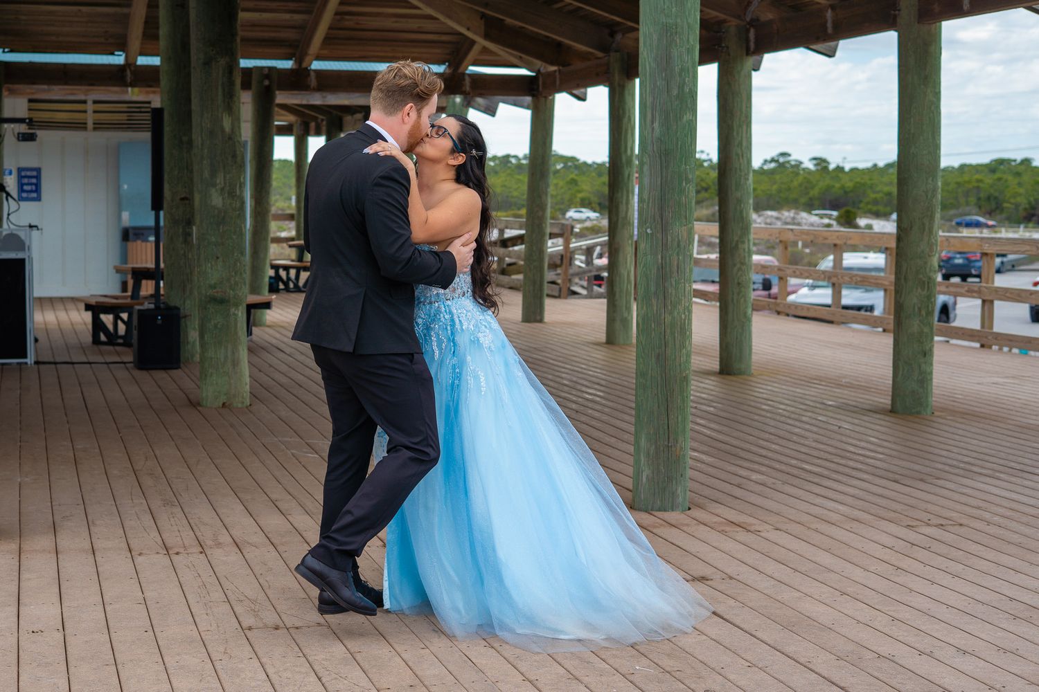 Couple sharing a romantic dance on a wooden deck, woman in elegant blue tulle ball gown.