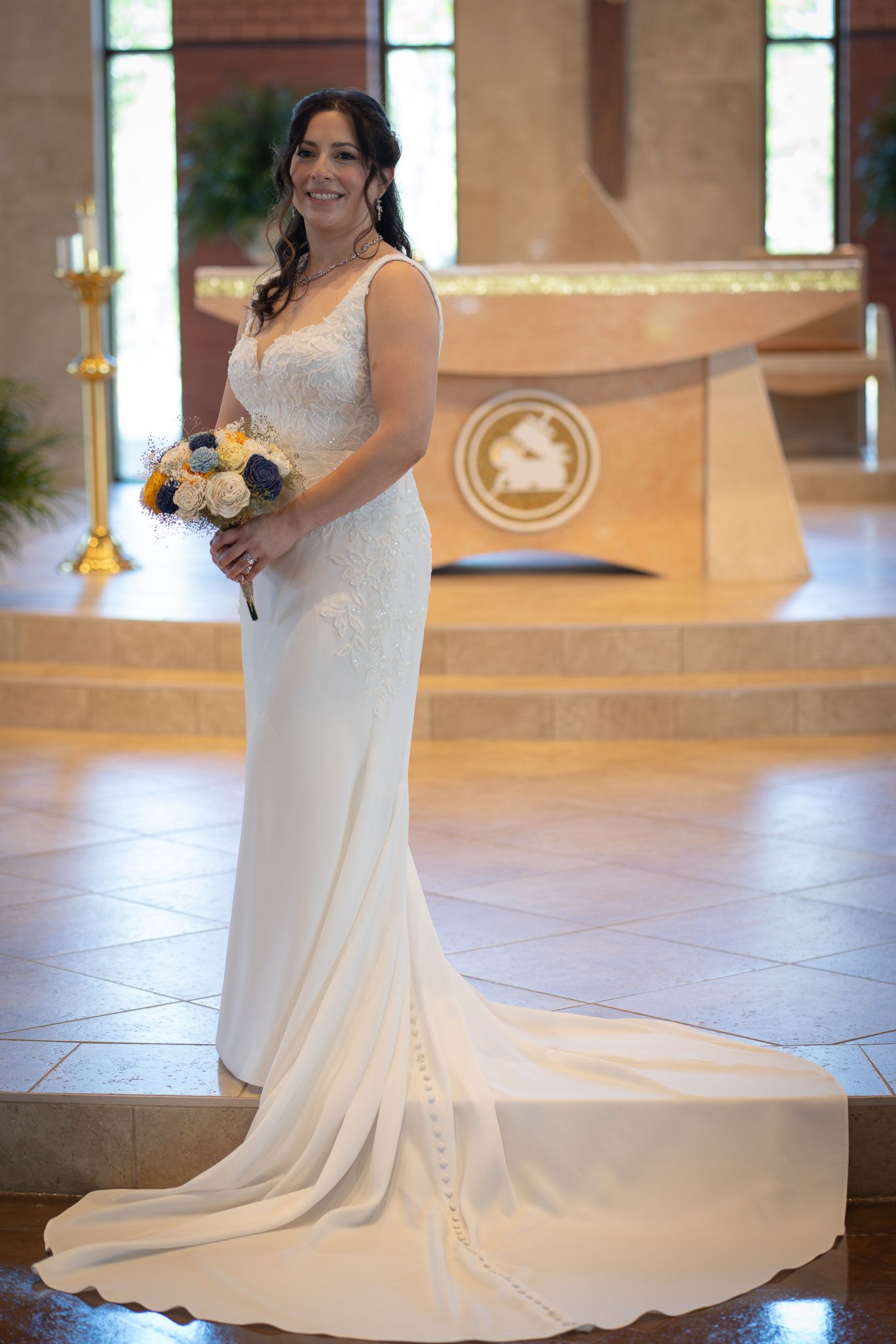 Bride in elegant fitted white gown with lace bodice holds bouquet inside a church.