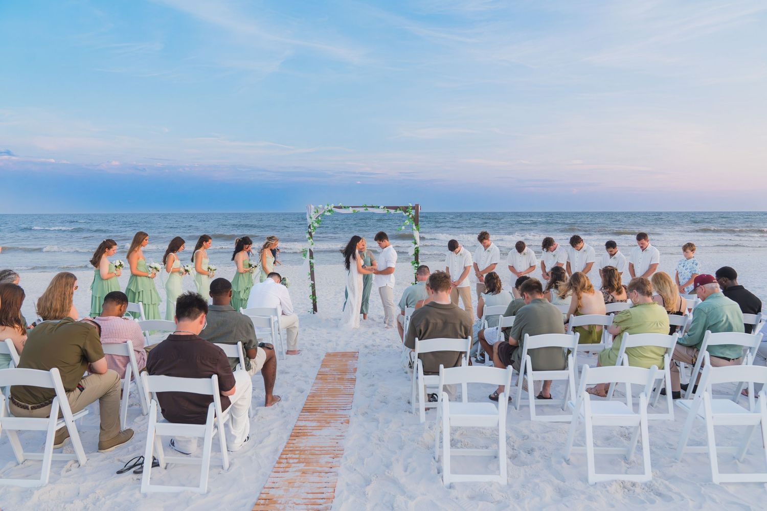 Romantic beach wedding ceremony at sunset with white chairs and ocean backdrop.