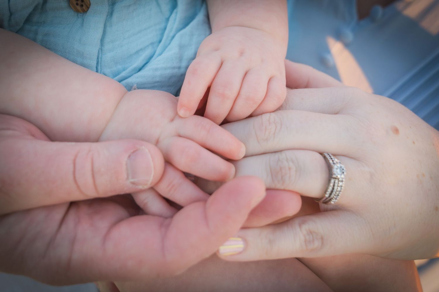 Close-up of baby and parents hands together, mother wearing diamond engagement ring, symbolizing family love.