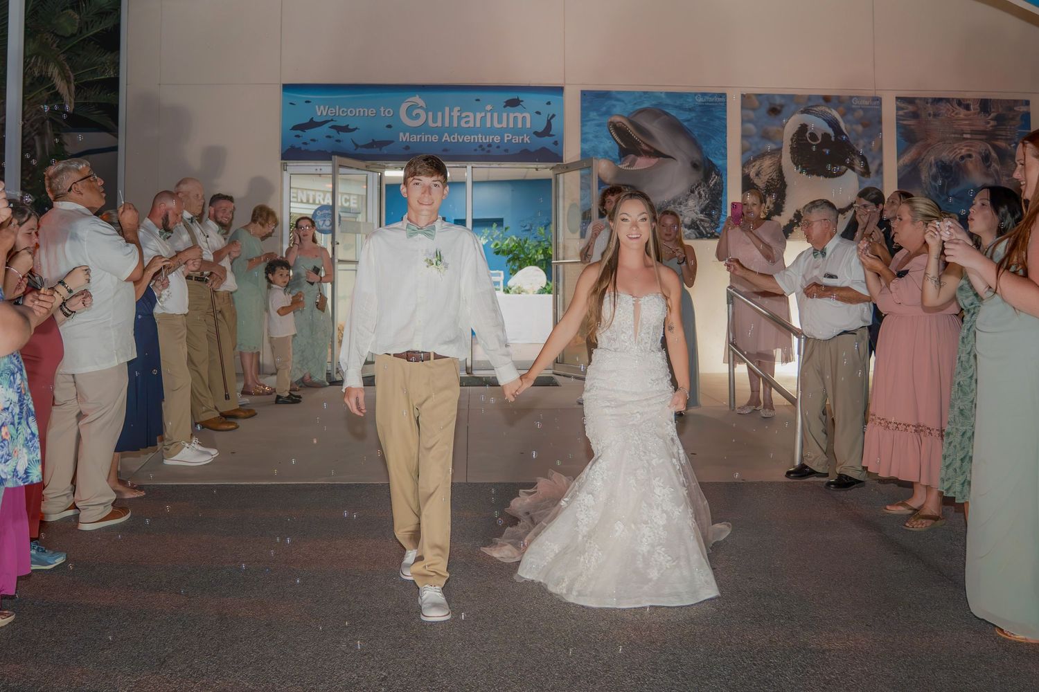 Newlyweds walk hand in hand through cheering guests outside Gulfarium venue at night wedding grand exit.